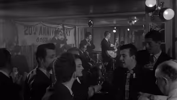 A woman and several men sit among patrons in a crowded nightclub