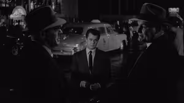 Sidney Falco (Tony Curtis) stands between two men in hats at night