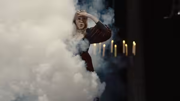 Woman in striped dress amid white smoke near rows of candles