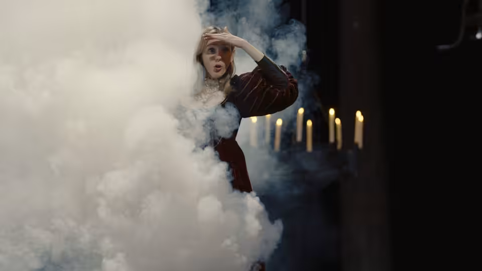 Woman in striped dress amid white smoke near rows of candles