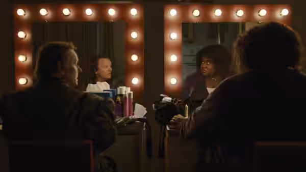Four people in a dressing room with two facing large lit mirrors