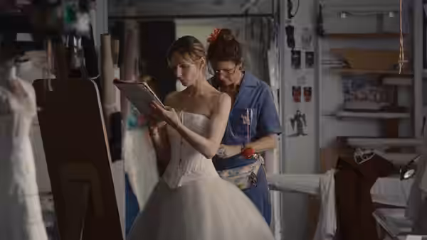 Woman in wedding dress checks tablet as another leans over her shoulder in fitting room