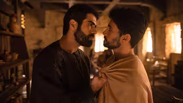 Two men face each other closely indoors one gripping the other's shoulder