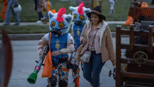 A woman walks beside two people wearing colorful animal masks