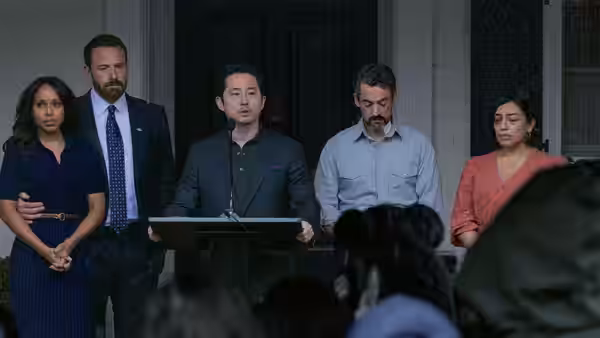 A man speaks at a lectern as four adults stand before an audience