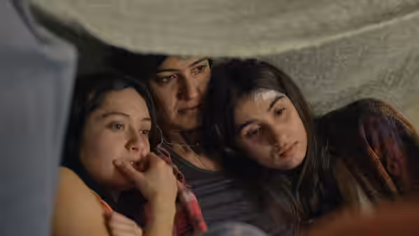Three women lying together under a blanket looking towards the camera