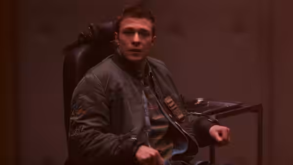 Thomas (Ruaridh Mollica) sits in a chair, turning toward someone nearby