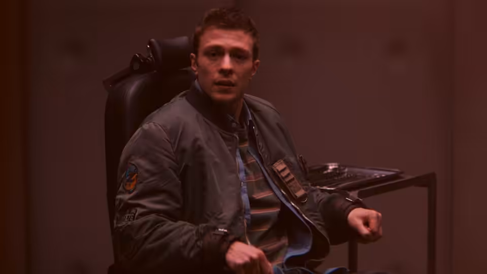 Thomas (Ruaridh Mollica) sits in a chair, turning toward someone nearby