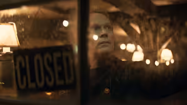 A man looks out from behind a closed sign on a rainy night