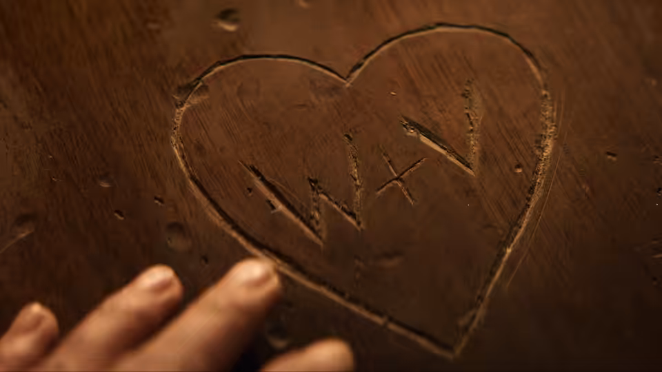 A hand reaches toward a heart carved into a wooden surface