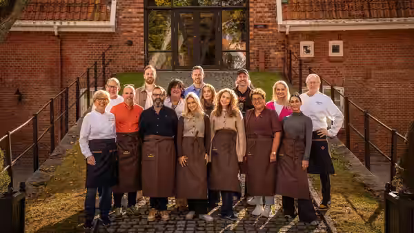 A group of cooks and teachers gathers outside a brick school building