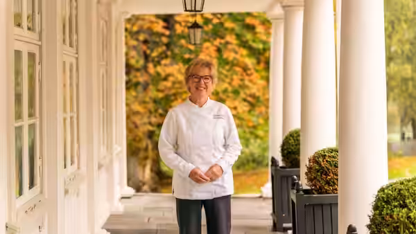 Wenche Andersen stands in her chef's jacket on a columned veranda