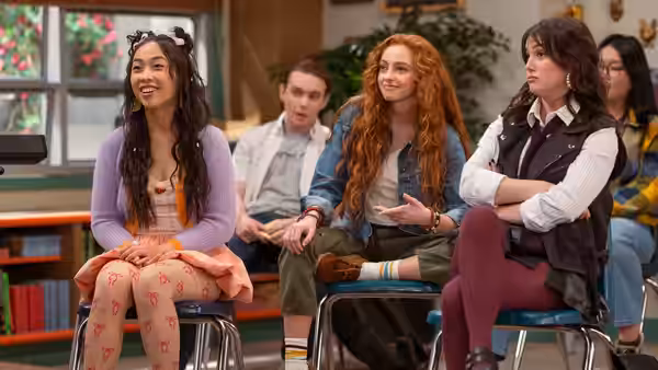 students sit at desks in a classroom as redhead gestures while talking