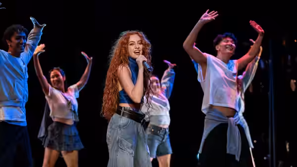 red-haired singer performs into microphone on stage with backup dancers