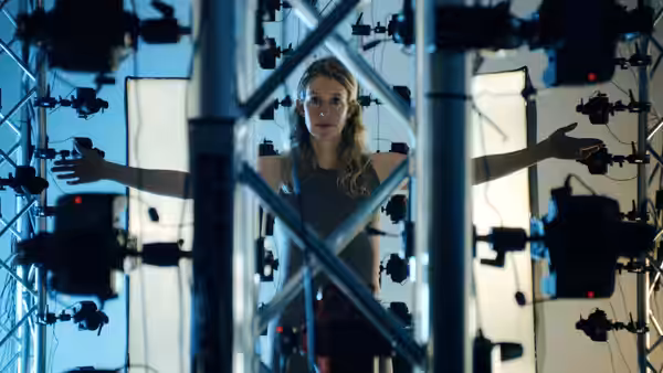 A woman stands among camera rigs with her arms extended between illuminated panels