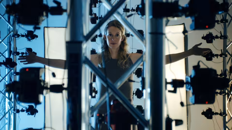 A woman stands among camera rigs with her arms extended between illuminated panels