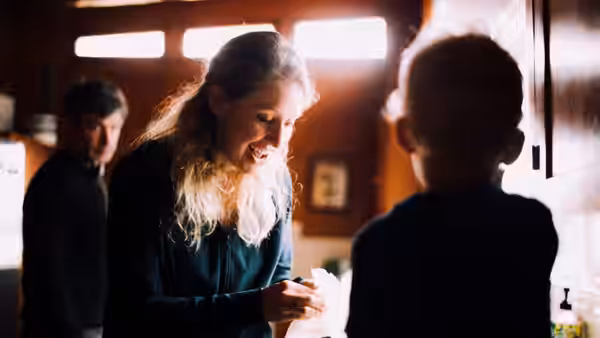 Smiling woman holds a tissue while speaking to a young boy in a kitchen