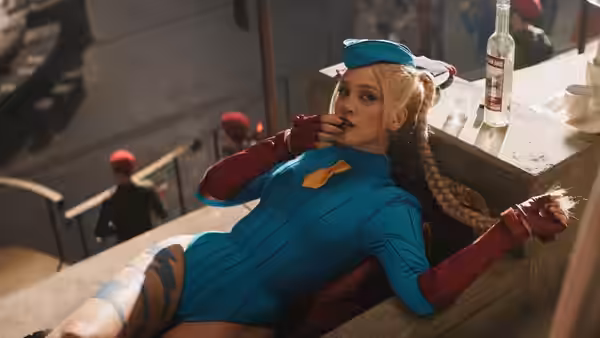 Cammy (Mel Jarnson) reclines beside a bar counter as red-capped guards stand below