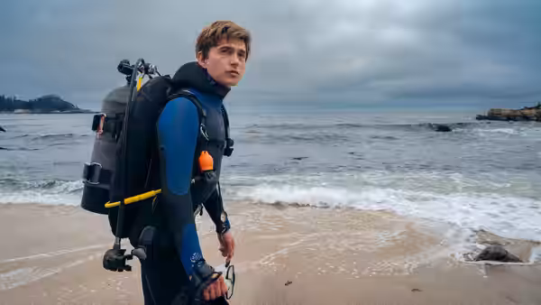 Jay Gardiner (Austin Abrams) in scuba gear standing on the beach