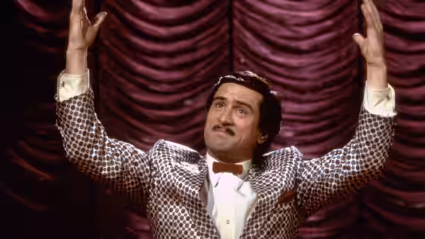 Rupert Pupkin on stage with arms raised wearing a patterned jacket