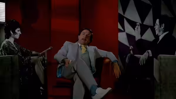 Rupert Pupkin reclining in a red armchair between a woman and a man