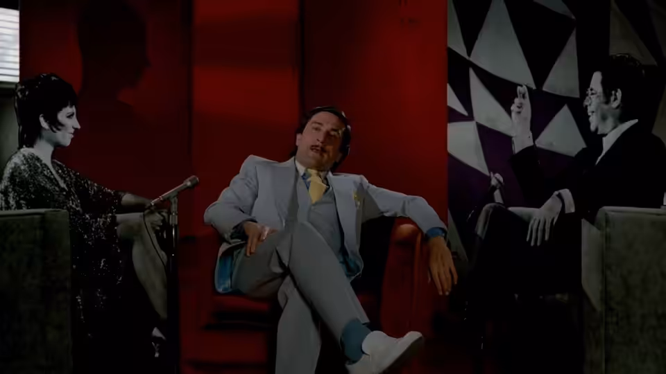 Rupert Pupkin reclining in a red armchair between a woman and a man