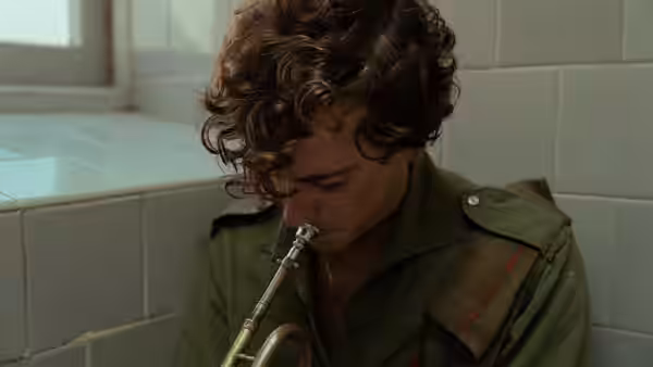 Young man plays trumpet while seated in tiled room