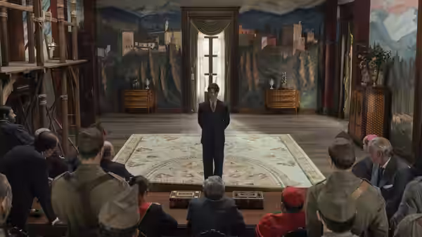 Man in suit stands before seated audience in muraled hall