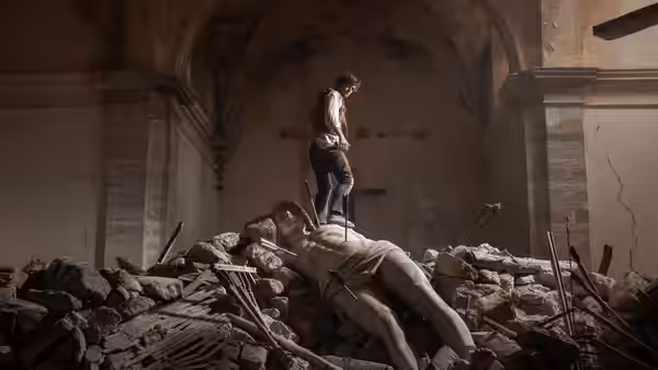 Man stands on rubble gazing down at a fallen statue
