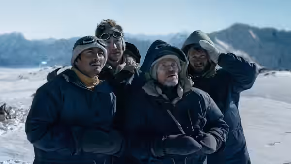 Four bundled mountaineers stand together on the snow, looking toward the mountains