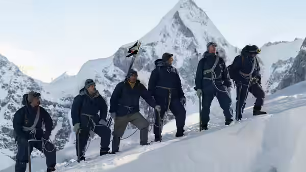 A line of mountaineers climbs a snowy slope beneath towering peaks