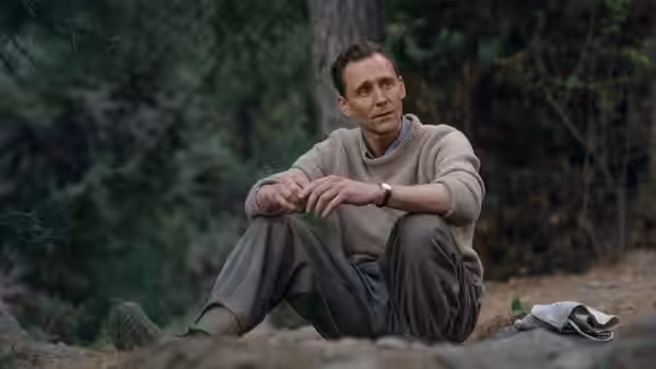 A man in a sweater sits resting on the ground among trees