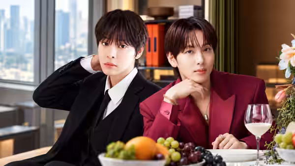 Two men sit at a dining table with fruit and wine