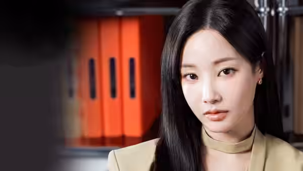 A woman in a beige jacket sits beside orange binders