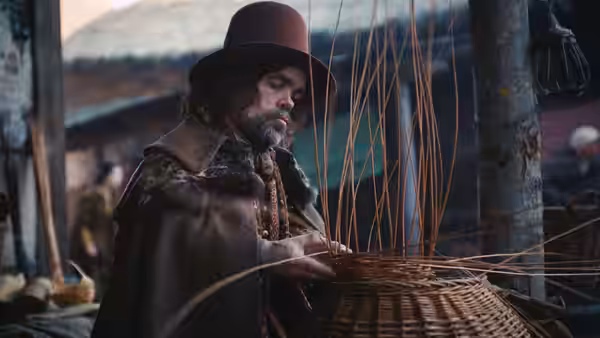 Basket Weaver (Peter Dinklage) crafting large wicker basket at outdoor market stall