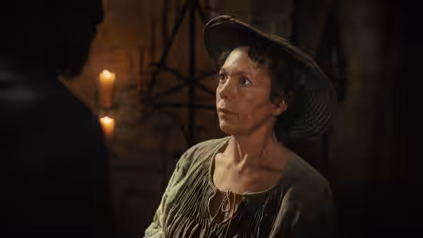 Fisherwoman (Olivia Colman) in hat looking up at dark figure indoors by candlelight