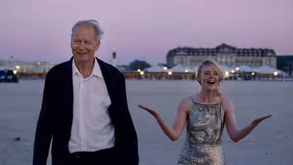 Rachel Kemp (Elle Fanning) gesturing on the beach beside an older man