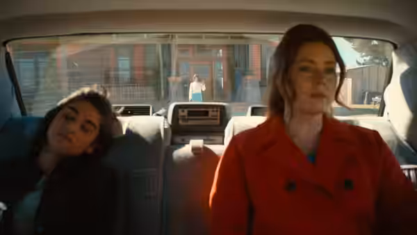 A woman in a red coat rides in a car beside a sleeping girl