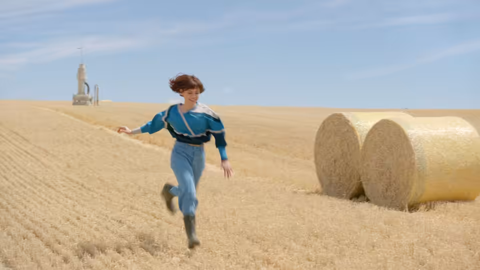 Klara (Jenna Ortega) running through a harvested field past hay bales