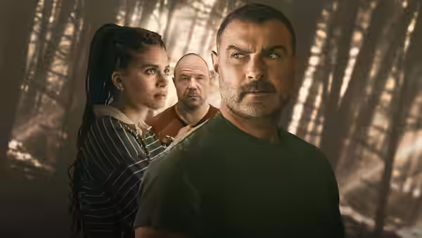 A man in a dark shirt stands before a woman and a bald man among trees