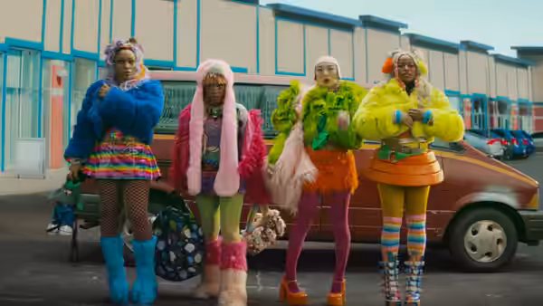 Four women in bright colorful outfits stand together by a parked car