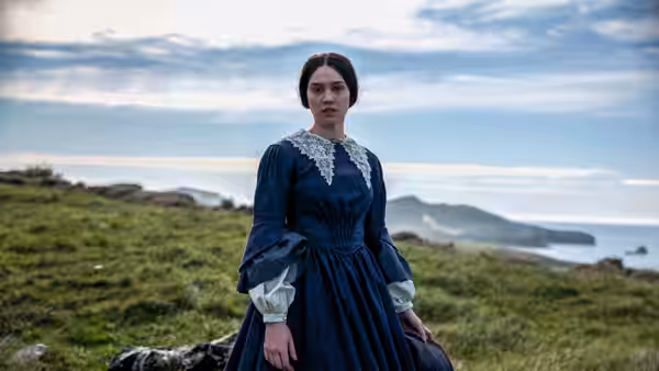 a woman in a blue dress standing on a grassy hill by the ocean