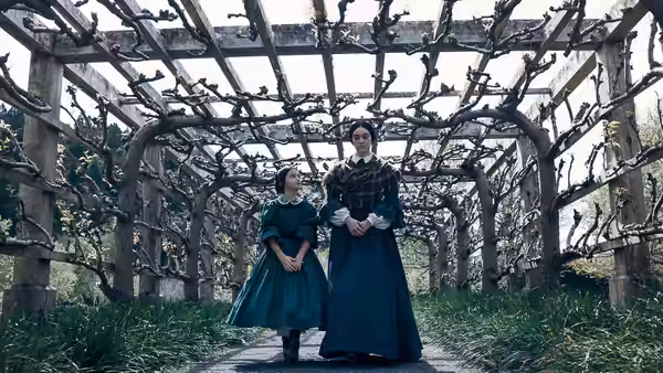 two women standing under a wooden pergola covered in bare vines