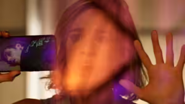 A woman raises her hand to block bright light from a phone