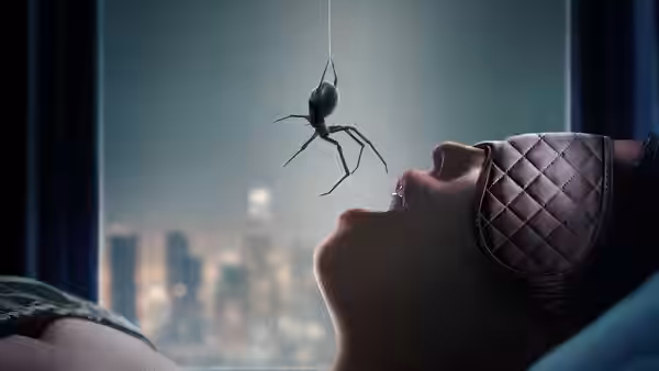 A woman lies in bed as a spider hangs above her open mouth