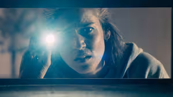 A woman holds a flashlight and stares ahead with wide eyes