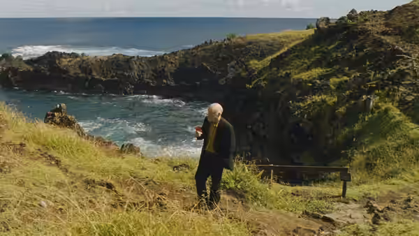 Chris (John Malkovich) walks along a grassy coastal path above the rocky shore