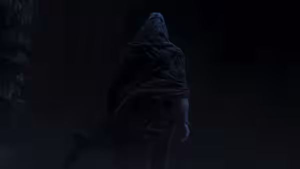 A hooded figure walks through a dim stone passage