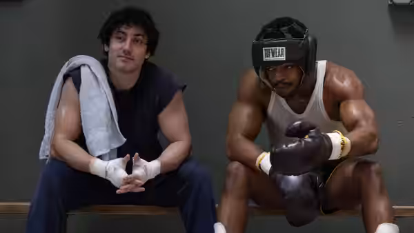 Sylvester Stallone (Anthony Ippolito) sits beside a boxer in a training room