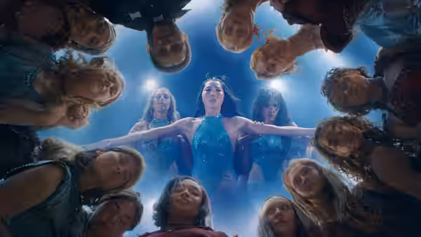 A woman in a blue dress extends her arms as a group peers down around her
